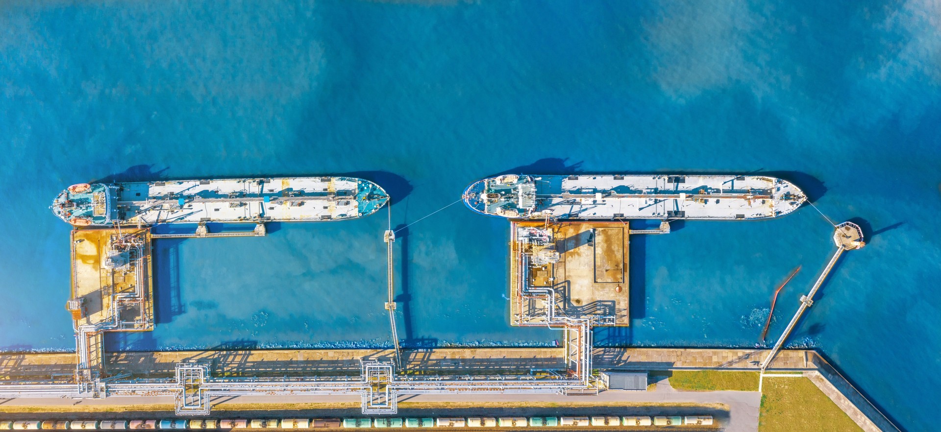 Aerial top view wide panorama of the oil terminal and two moored tankers with liquid fuel loaded on the pier, railway tank cars for loading and unloading.